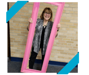 Cheryl in a pink mirror frame standing in front of a brick wall