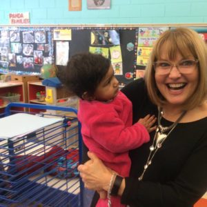 A teacher smiles and laughs at Glendale Heights Child Care in Glendale, WI as she holds a child in pink