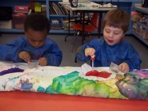 Two young children using watercolor to paint a roll of white paper at Glendale Heights Child Care in Glendale, WI